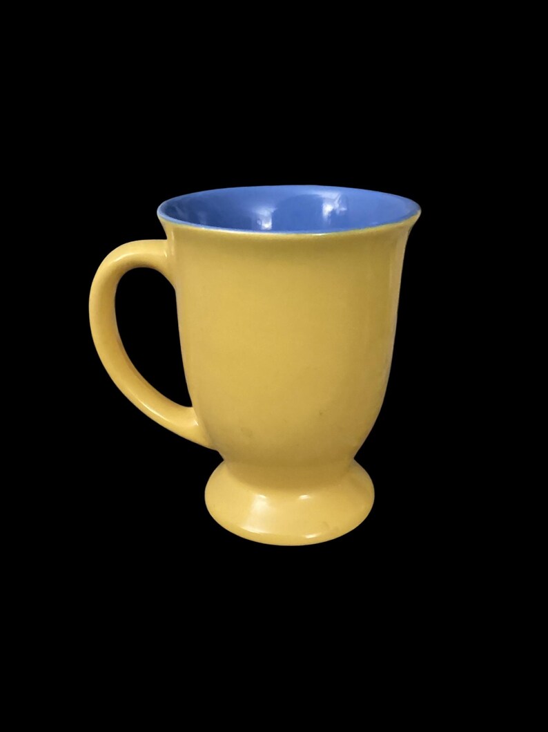 May include: A yellow ceramic mug with a blue interior. The mug has a wide base and a handle.