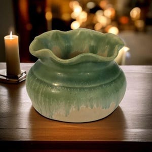 May include: A green ceramic planter with a ruffled rim. The planter has a light green glaze with white streaks and a white base.