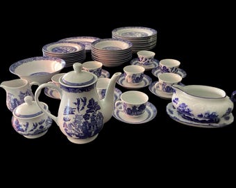 May include: A large dinnerware set featuring white porcelain with a blue willow pattern. The collection includes a teapot, creamer, sugar bowl, gravy boat, multiple cups with saucers, bowls, and stacked dinner plates, all with matching blue designs.