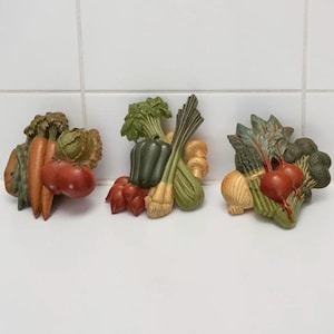 May include: Three decorative vegetable clusters. The first features carrots, tomatoes, and a cabbage. The second includes a green pepper, leeks, and mushrooms. The third showcases onions, beets, asparagus, and broccoli. Each cluster is painted with realistic colors.