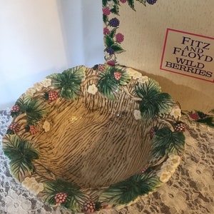 May include: A ceramic bowl with a brown and green design featuring wild berries and white flowers. The bowl is made by Fitz and Floyd and is part of their Wild Berries collection.