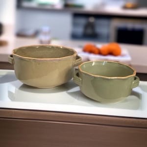 May include: Two ceramic bowls with handles. The larger bowl is beige and the smaller bowl is green.