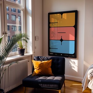 K&ouml;nnte beinhalten: Ein gerahmter Kunstdruck mit schwarzem Rahmen, der drei gestapelte, farbige rechteckige Formen in Gelb, Koralle und Blau zeigt. Das Wort "YAY!" steht unten. Ein marineblauer Stuhl mit einem orangefarbenen Kissen steht daneben.