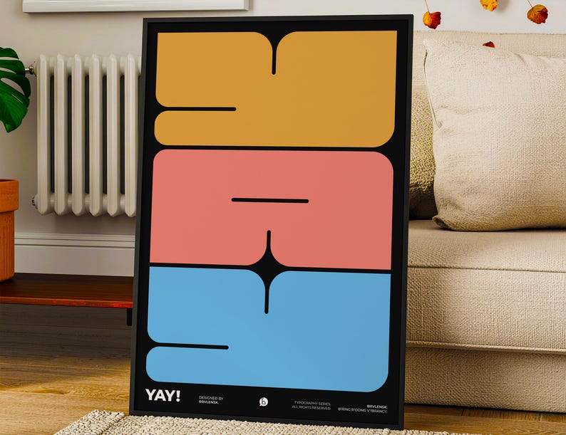 K&ouml;nnte beinhalten: Ein gerahmter Kunstdruck mit dem Wort "YAY!" in gro&szlig;en, farbenfrohen, abstrakten Formen. Das Design zeigt einen schwarzen Hintergrund mit gestapelten Bl&ouml;cken in Orange, Koralle und Blau. Der Druck wird in einem Wohnzimmer gezeigt.