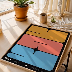 K&ouml;nnte beinhalten: Ein gerahmter Kunstdruck mit modernem Design. Er zeigt drei horizontale Bl&ouml;cke in Gelb, Koralle und Blau auf schwarzem Hintergrund. Das Wort "YAY!" ist wei&szlig; gedruckt. Der Druck wird auf einem Holztisch in der N&auml;he eines Fensters pr&auml;sentiert.