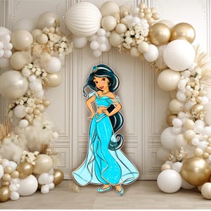 May include: A cutout of a cartoon character with long black hair, wearing a light blue off-the-shoulder top and matching harem pants with gold trim, standing in front of an archway decorated with white, cream, and gold balloons.