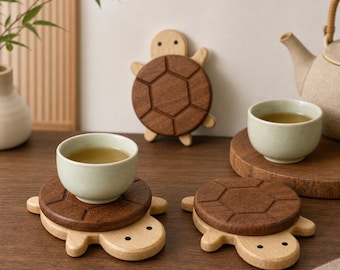 May include: Three wooden turtle-shaped coasters featuring a light-colored head and limbs with a dark brown, hexagonal-patterned shell. Two coasters support light green ceramic tea cups, while one stands upright in the background.
