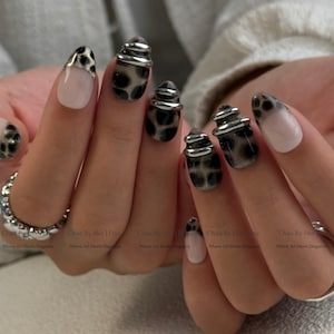 May include: A close-up of a hand with a manicure featuring a mix of designs. Some nails are painted with a leopard print, others are a light pink with silver accents. Some nails have a 3D silver design. The text "Chae By Her" is visible.