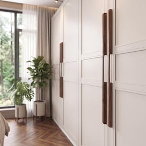May include: A set of long, vertical, dark brown wooden cabinet handles mounted on large, off-white, paneled wardrobe doors. The handles feature a smooth, rectangular design with rounded edges, contrasting against the light-colored door surface.