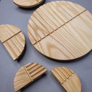 Op de afbeelding: Een verzameling lichtgekleurde houten serveerschalen en decoratieve stukken. De schalen zijn rond en halfrond, met een groefontwerp. De houtnerf is zichtbaar en de stukken zijn gerangschikt op een grijze ondergrond.