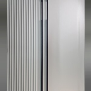 May include: A close-up of a white door with two long, black handles. The left side of the door has vertical, ridged detailing, while the right side is smooth with subtle linear accents. The handles are sleek and modern.