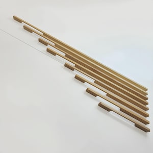 May include: Angled view of several light brown wooden cabinet pulls with a rectangular design. The pulls are arranged in a diagonal pattern against a white background, suggesting a modern aesthetic.