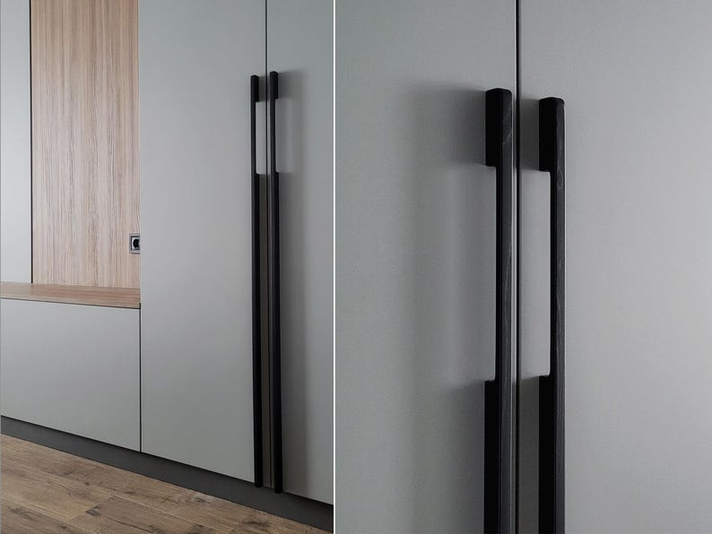 May include: Close-up of a modern cabinet with two long, black handles. The handles are rectangular and have a sleek, minimalist design. The cabinet doors are a light gray color, and the background includes a wooden panel and a light-colored wall.