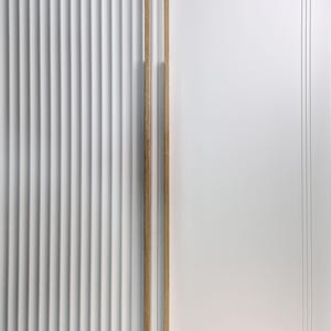 May include: A white door with vertical ribbed paneling on the left and a smooth white panel on the right. Two vertical wooden door pulls are mounted on the right panel. The door pulls are made of light-colored wood.