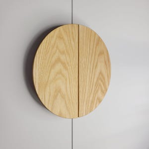 May include: A light-colored, wooden cabinet door with a circular design. The door is split into two halves, with a vertical seam down the middle. The wood grain is visible, and the door is mounted on a white surface.