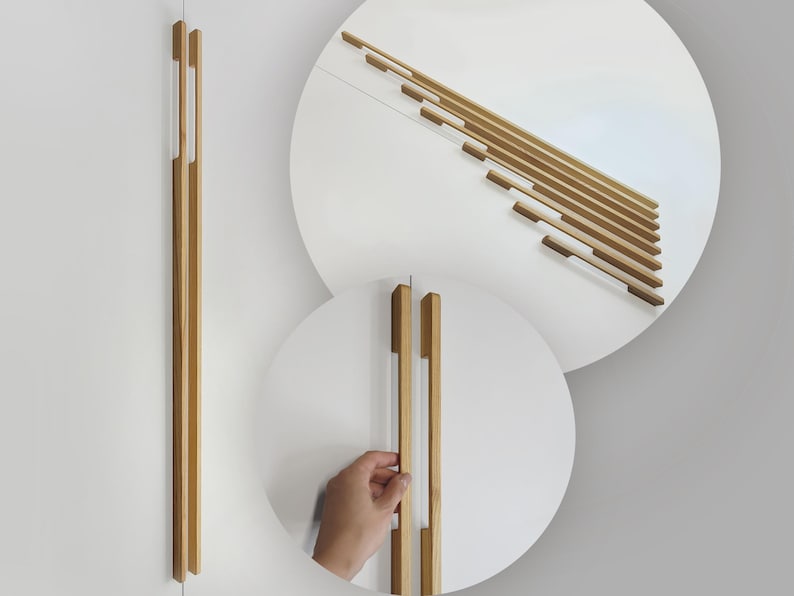 May include: Wooden cabinet pulls in a light brown color. The pulls are long and rectangular, with a modern design. The image also shows a close-up of the pulls on a white cabinet door. The pulls are approximately 12 inches long.