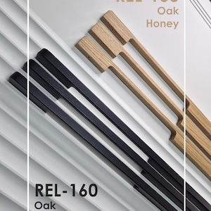 May include: An overhead shot of cabinet pulls in two colors, black and oak honey. The pulls are rectangular with a handle. The text "REL-160 Oak Black" and "REL-160 Oak Honey" is displayed in the image.