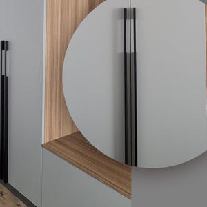 May include: Close-up of modern cabinet hardware. The image shows a gray cabinet with a long, black handle. The handle is a sleek, vertical design. The cabinet has a wood grain accent. The overall aesthetic is minimalist and contemporary.