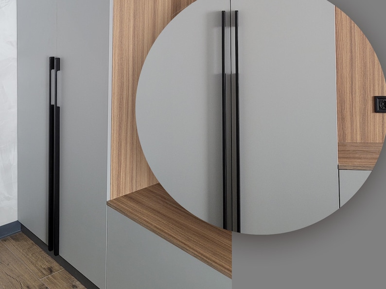 May include: Close-up of modern cabinet hardware. The image shows a gray cabinet with a long, black handle. The handle is a sleek, vertical design. The cabinet has a wood grain accent. The overall aesthetic is minimalist and contemporary.