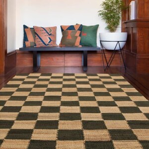 May include: A woven area rug with a checkerboard pattern in shades of green and tan. A black bench with decorative pillows in various colors sits against a wood-paneled wall. A white planter with a plant is also visible.