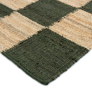 May include: Close-up of a woven rug with a checkerboard pattern. The rug features alternating squares of dark green and natural beige. The texture of the rug appears to be made of a natural fiber.