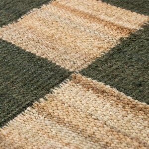 May include: Close-up of a woven rug with a checkerboard pattern. The squares alternate between a dark green and a natural beige color. The rug has a textured, nubby surface.