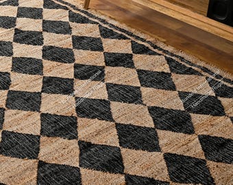 May include: A rectangular area rug featuring a repeating diamond pattern in alternating black and natural tan fibers. The rug has a textured, woven construction with a visible fringe edge along the border, creating a geometric visual effect.