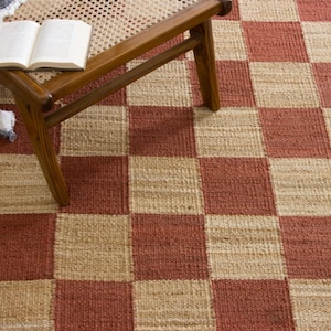May include: A woven area rug with a red and beige checkerboard pattern. A wooden bench with a woven seat and a book are in the upper left corner. The rug is made of natural fibers.