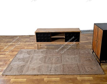 Puede incluir: Una alfombra rectangular con una textura tejida en color tostado natural y un patrón geométrico de cuadrados repetidos. La alfombra se sitúa sobre un suelo de madera frente a un mueble bajo de madera con puertas negras y estante.