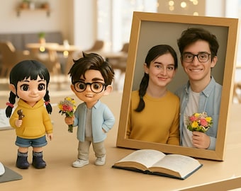 Op de afbeelding: Een houten fotolijst met een lachend stel, twee cartoonbeeldjes en een open boek op een lichtbruin oppervlak. De beeldjes zijn van een meisje in een gele hoodie en een jongen met bloemen. De fotolijst is schuin.