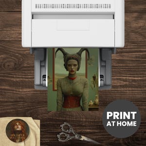 May include: A printer is shown printing a portrait of a woman with horns, wearing a green dress and red corset. The image is on a wooden surface with a round sticker that says "HRAETH MACABRE" and a pair of decorative scissors.