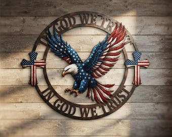 May include: A circular wall sign featuring a bald eagle with wings spread, colored in red, white, and blue. The eagle is centered within a dark frame inscribed with the text IN GOD WE TRUST. Two crosses with American flag patterns flank the eagle.