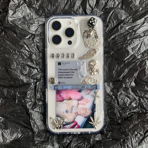 May include: Clear phone case with a variety of silver charms, including a skull, wings, and a butterfly. The case also features a photo and the text "GUILD" and "Virgo".
