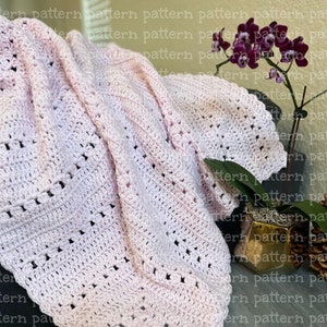 May include: A pink crocheted baby blanket with a delicate stitch pattern. The blanket is folded and draped over a wooden surface.