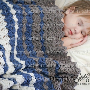 May include: A white, blue, and gray crocheted baby blanket with a scalloped edge. The blanket is draped over a white surface with a sleeping child underneath. The text "Baby Knits" is visible in the lower right corner of the image.