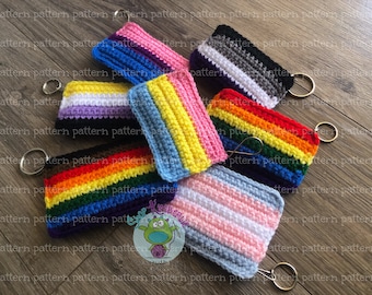 May include: A set of crocheted keychains featuring different pride flags, including the rainbow, transgender, bisexual, and asexual flags. Each keychain is attached to a gold metal ring.