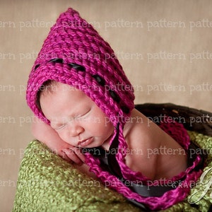May include: A sleeping baby wearing a pink crocheted hat with black trim. The baby is lying on a green crocheted blanket.
