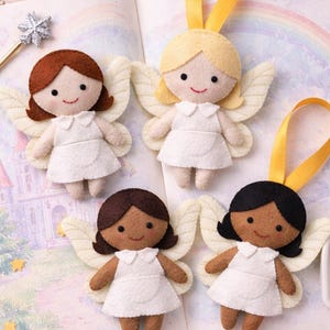 May include: Four felt angel ornaments with different hair colors and skin tones, each wearing a white dress and wings. They have yellow ribbon hangers. The angels are on a book with a rainbow illustration, surrounded by decorative stars and a pink satin bag.