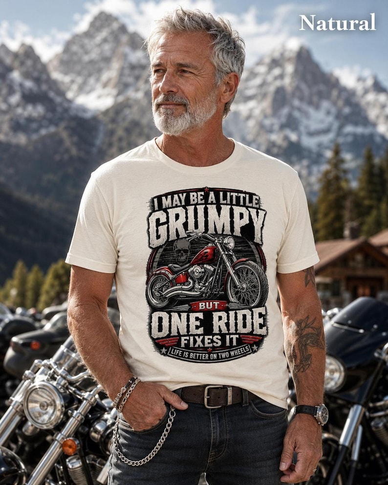 A man with a gray beard and tattoos wears a natural colored t-shirt with a red motorcycle graphic and the text "I MAY BE A LITTLE GRUMPY BUT ONE RIDE FIXES IT LIFE IS BETTER ON TWO WHEELS."