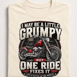 A folded natural colored t-shirt displays a red motorcycle graphic and the text "I MAY BE A LITTLE GRUMPY BUT ONE RIDE FIXES IT LIFE IS BETTER ON TWO WHEELS."