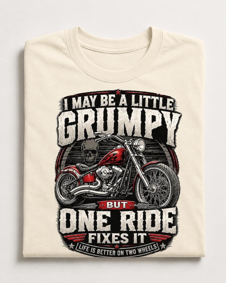 A folded natural colored t-shirt displays a red motorcycle graphic and the text "I MAY BE A LITTLE GRUMPY BUT ONE RIDE FIXES IT LIFE IS BETTER ON TWO WHEELS."