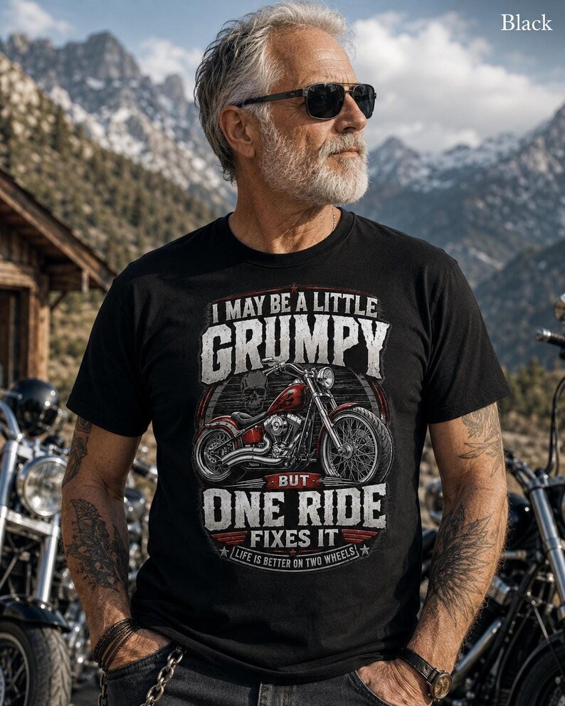 A man with a gray beard, sunglasses, and tattoos wears a black t-shirt with a red motorcycle graphic and the text "I MAY BE A LITTLE GRUMPY BUT ONE RIDE FIXES IT LIFE IS BETTER ON TWO WHEELS."