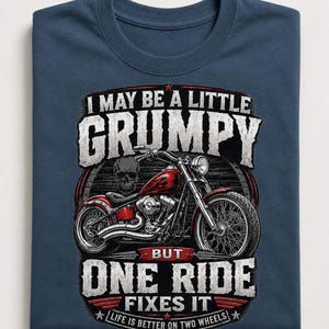 A folded navy blue t-shirt displays a red motorcycle graphic and the text "I MAY BE A LITTLE GRUMPY BUT ONE RIDE FIXES IT LIFE IS BETTER ON TWO WHEELS."