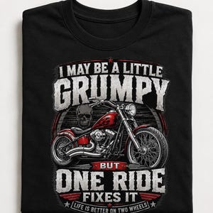 A folded black t-shirt displays a red motorcycle graphic and the text "I MAY BE A LITTLE GRUMPY BUT ONE RIDE FIXES IT LIFE IS BETTER ON TWO WHEELS."
