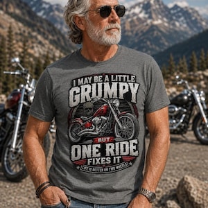A man with a gray beard, sunglasses, and tattoos wears a graphite heather t-shirt with a red motorcycle graphic and the text "I MAY BE A LITTLE GRUMPY BUT ONE RIDE FIXES IT LIFE IS BETTER ON TWO WHEELS."