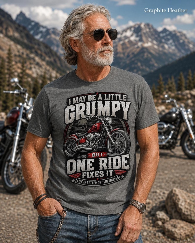 A man with a gray beard, sunglasses, and tattoos wears a graphite heather t-shirt with a red motorcycle graphic and the text "I MAY BE A LITTLE GRUMPY BUT ONE RIDE FIXES IT LIFE IS BETTER ON TWO WHEELS."