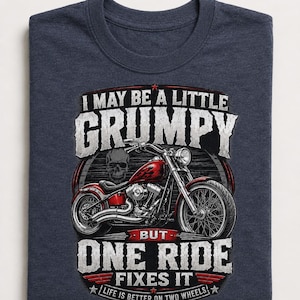 A folded heather navy t-shirt displays a red motorcycle graphic and the text "I MAY BE A LITTLE GRUMPY BUT ONE RIDE FIXES IT LIFE IS BETTER ON TWO WHEELS."