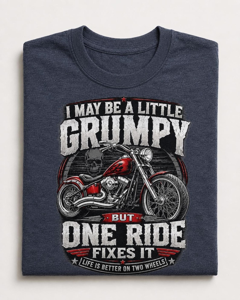 A folded heather navy t-shirt displays a red motorcycle graphic and the text "I MAY BE A LITTLE GRUMPY BUT ONE RIDE FIXES IT LIFE IS BETTER ON TWO WHEELS."