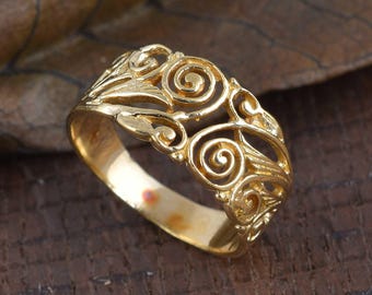 May include: A gold-colored ring with an openwork design featuring swirling, scroll-like patterns. The ring has a polished finish and a band that tapers towards the back. The ring is likely made of gold or a gold-toned metal.