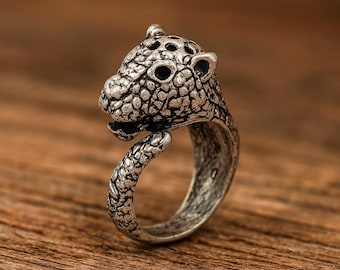 May include: A silver-toned ring with a detailed leopard head design. The ring's head is textured, with visible eyes, ears, and mouth. The band curves around to form the ring's base, creating a unique animal-themed jewellery piece.